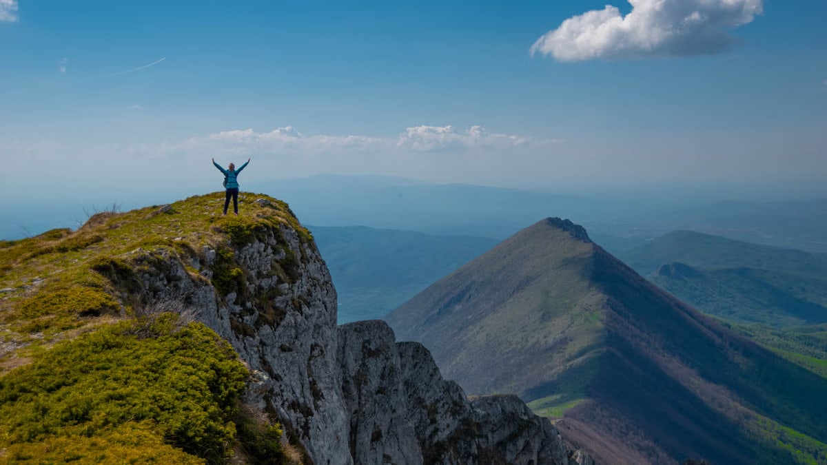 A person celebrating victory atop a mountain peak in Serbia with breathtaking views.